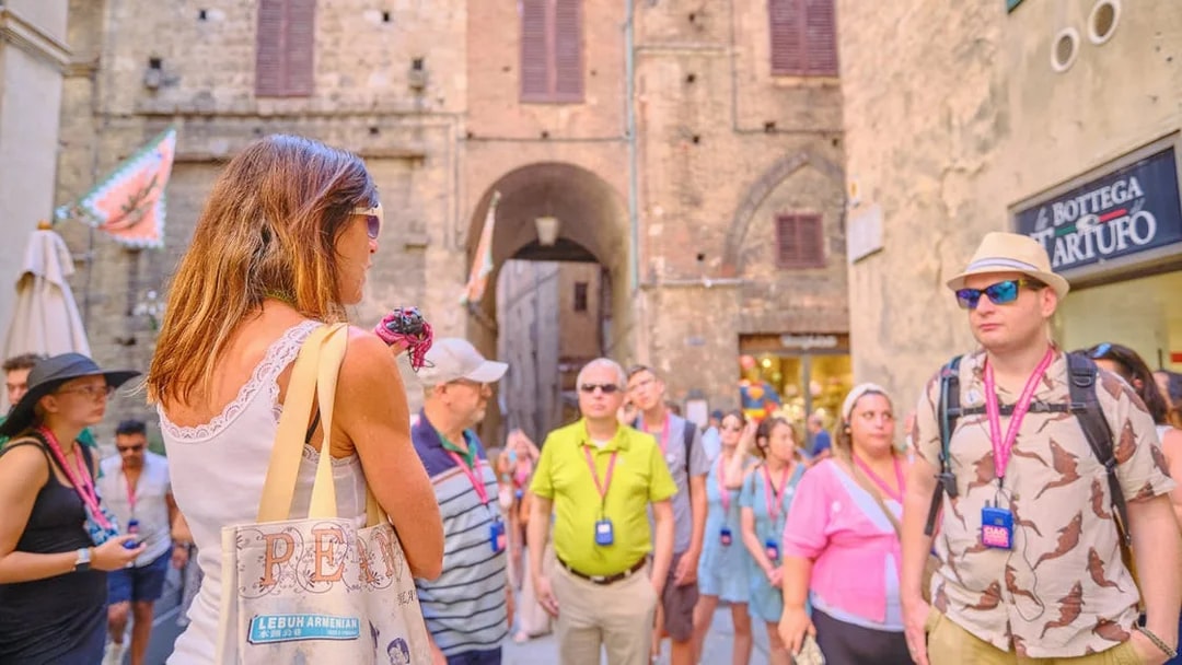Tour guide speaking to tourists in a historic street during Pisa, Siena, and San Gimignano day trip.