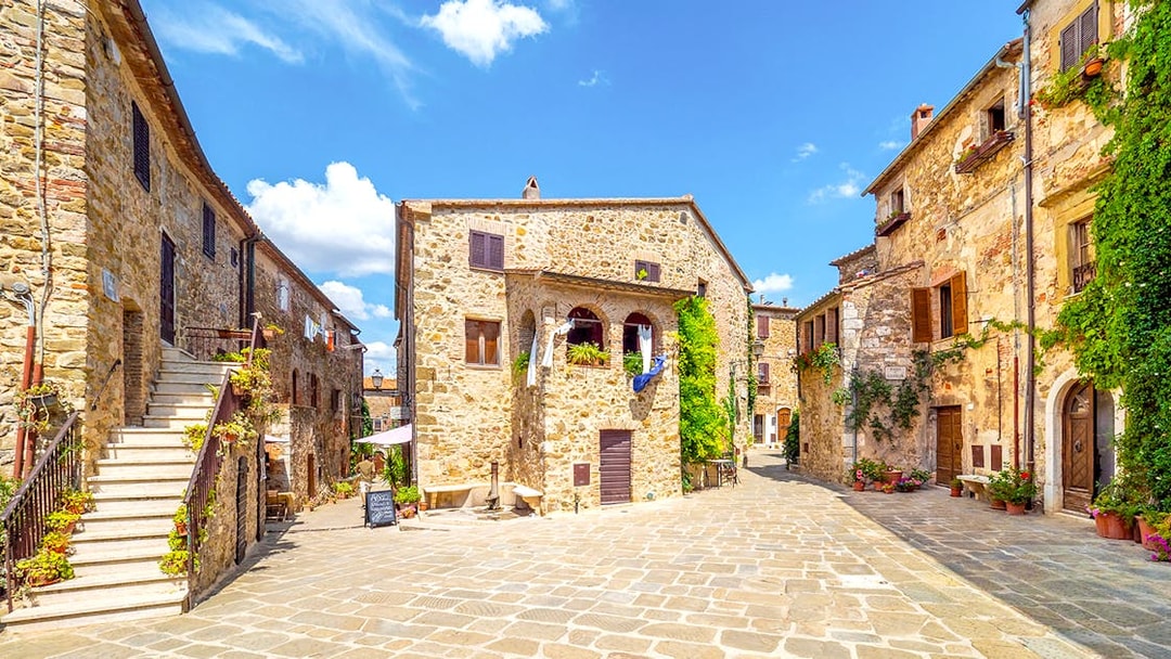 Stone buildings in a sunny Tuscan village square, part of the Highlights of Tuscany tour.