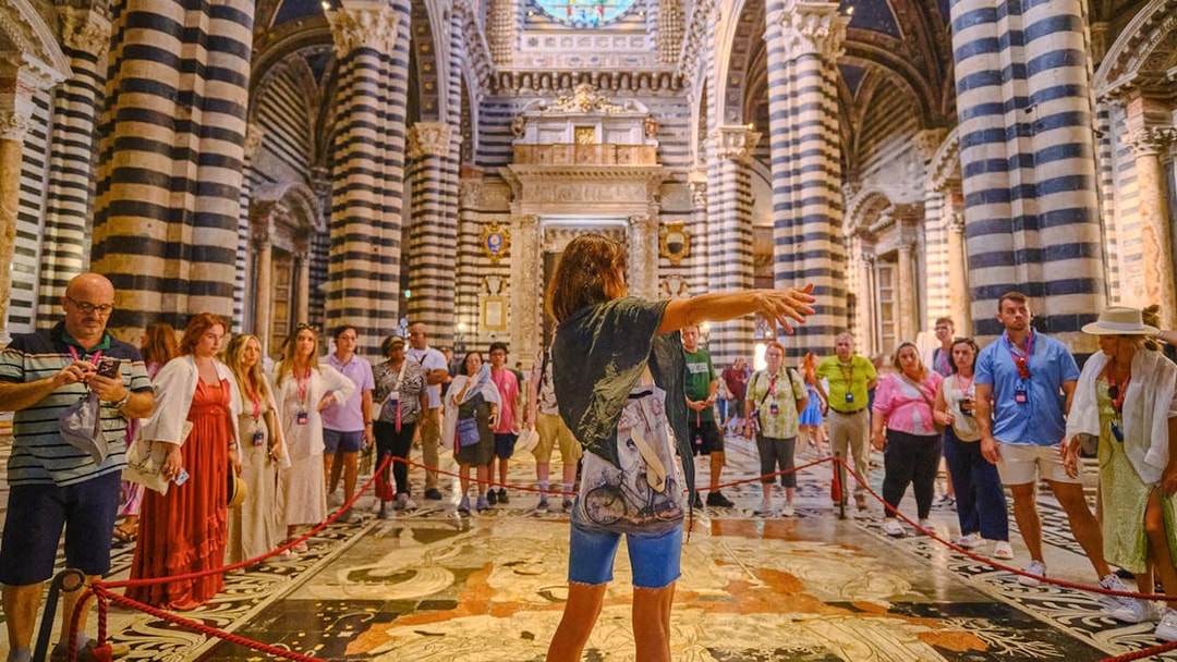 Tour group inside Siena Cathedral with striped columns and stained glass window.