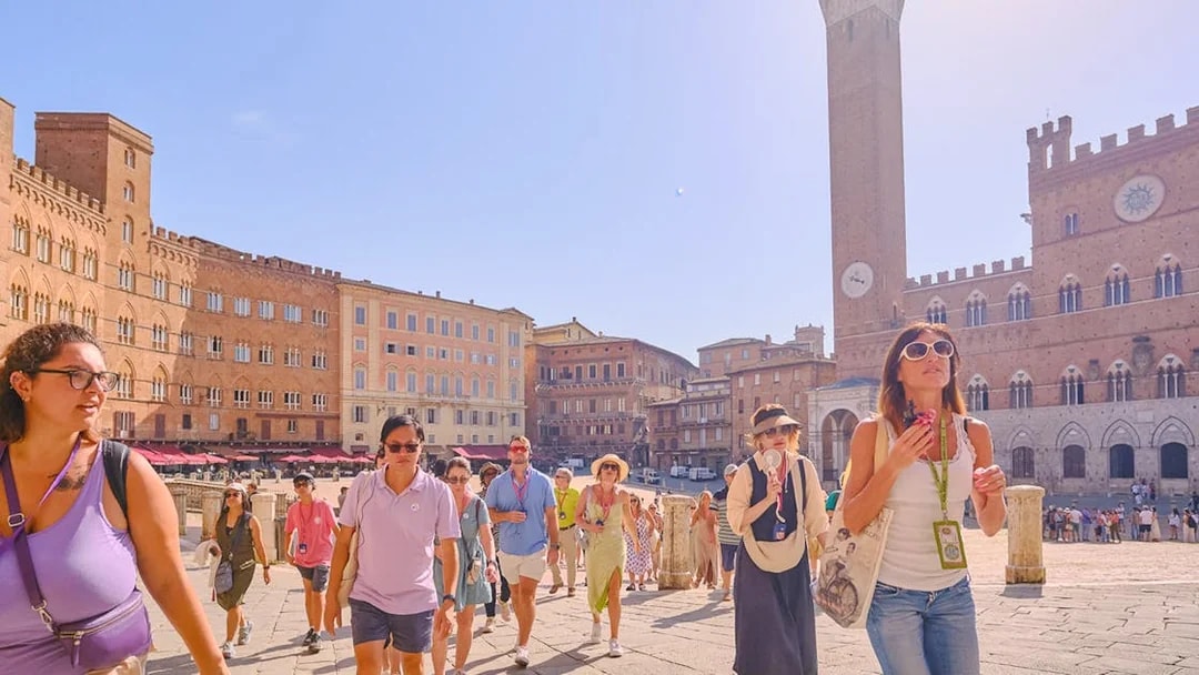 Tour group with guide at Piazza del Campo, Siena, Italy, with historic buildings in background.