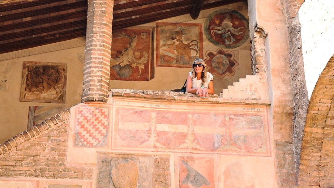 Woman on a historic balcony with frescoes in San Gimignano, Italy.