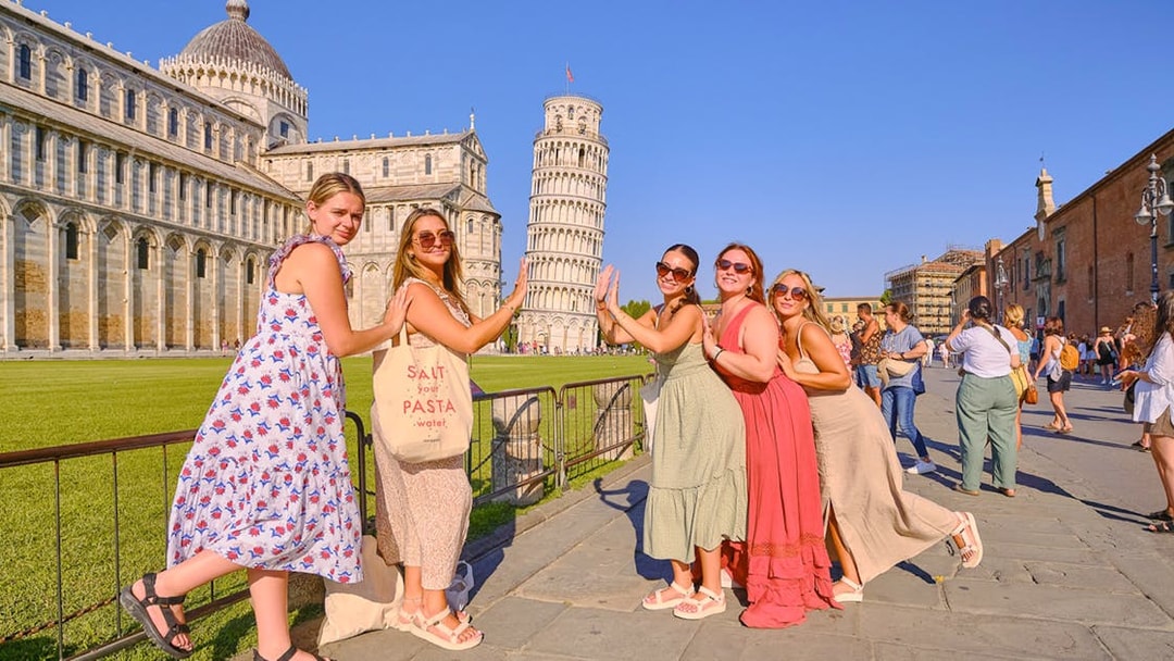 Women posing playfully with the Leaning Tower of Pisa in Italy.