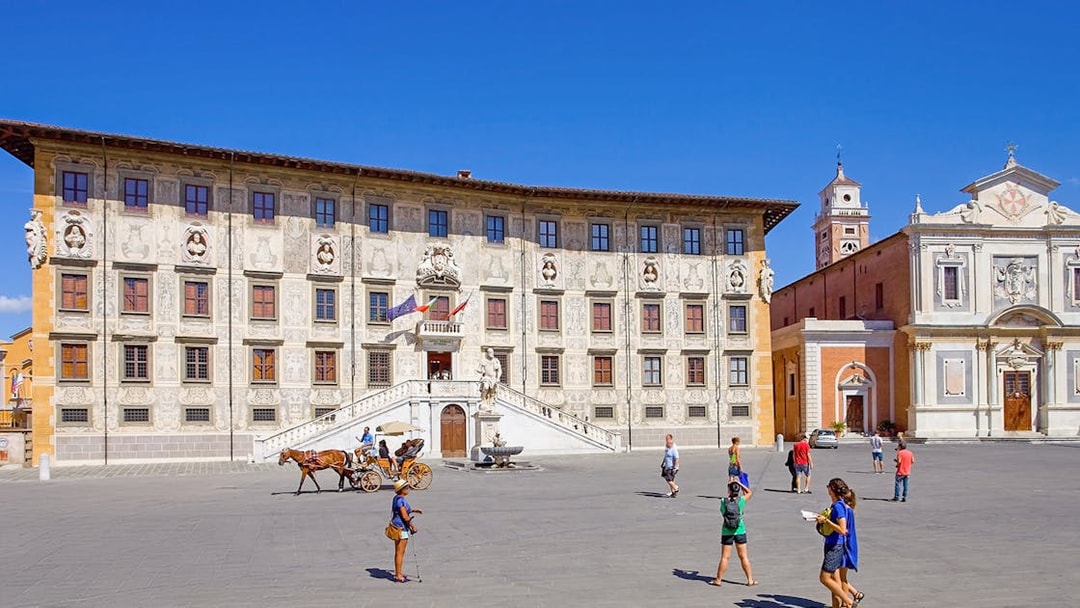 Scuola Normale Superiore at Piazza dei Cavalieri, Pisa, with tourists and a horse-drawn carriage.