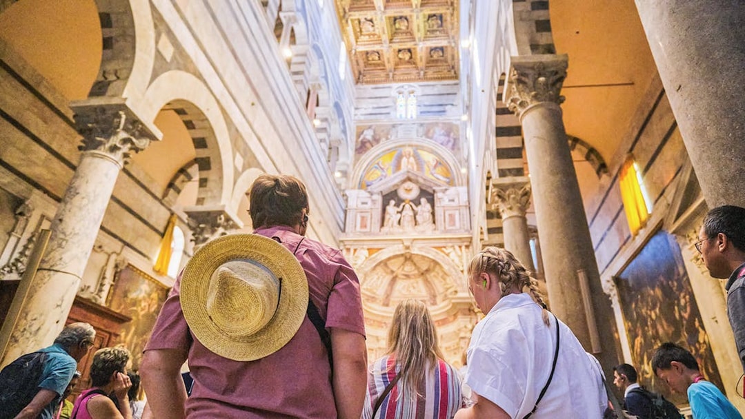 Visitors inside Pisa Cathedral, Italy, admiring ornate ceiling and arches.