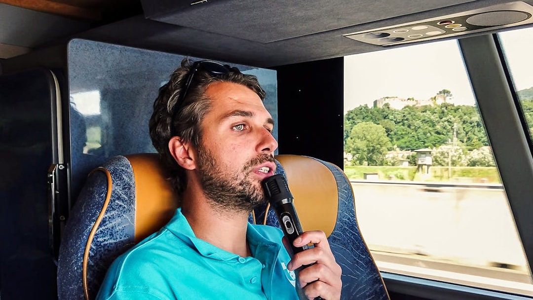 Tour guide speaking into a microphone on a bus during a guided tour from Florence to Pisa.
