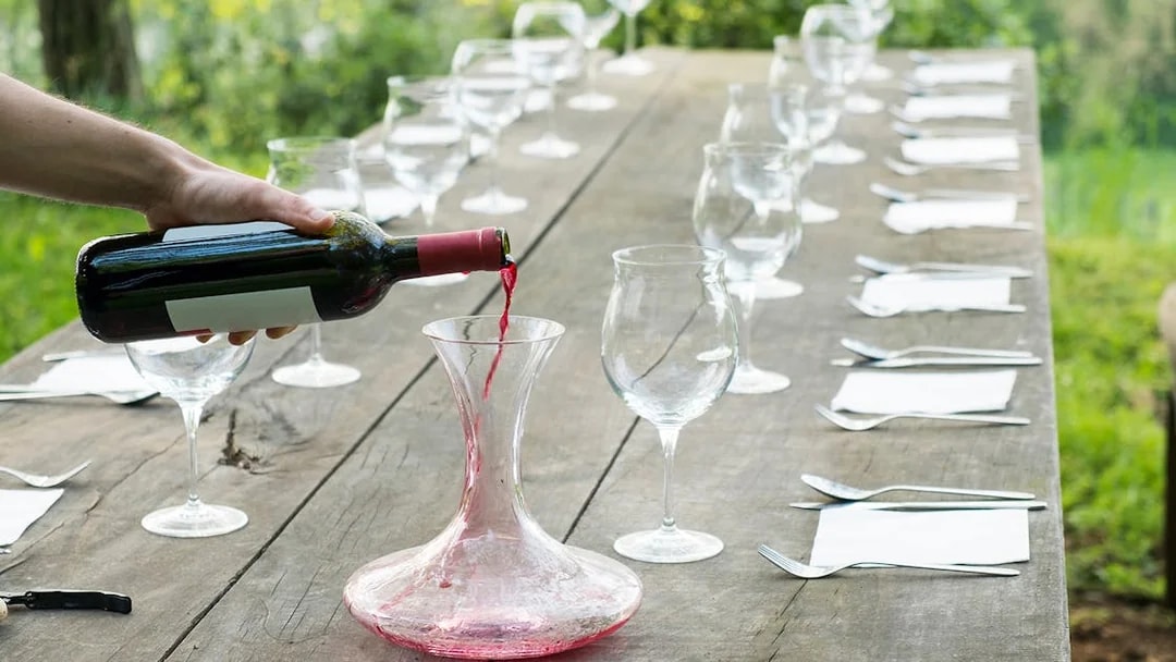 Pouring red wine into a decanter on a rustic table set for a Tuscany wine tour.