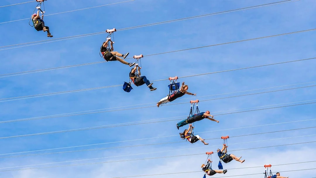Zipliners soaring on Fly LINQ Zipline in Las Vegas against a clear sky.