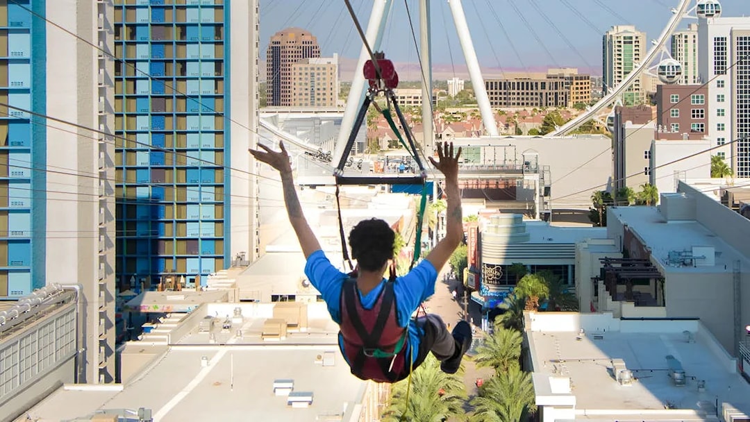 Person ziplining over Las Vegas with cityscape and High Roller observation wheel in view.