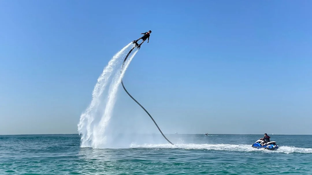 Flyboarding over the sea in Dubai with a jet ski nearby.