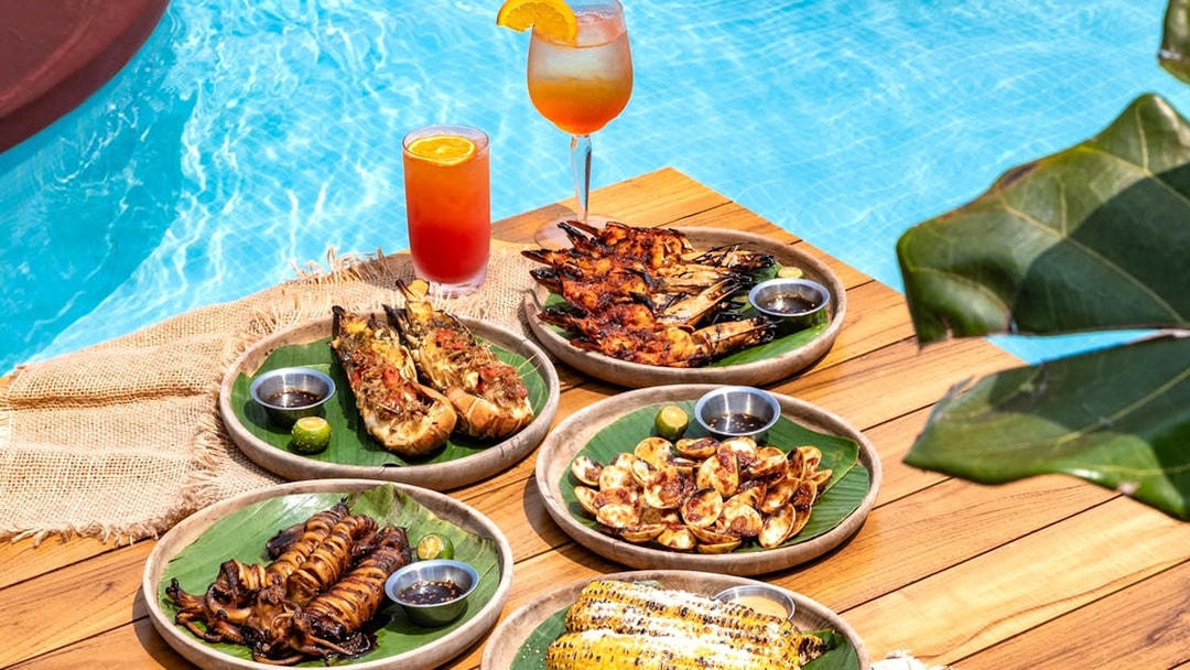 Grilled seafood and tropical drinks by a pool, part of Food Discovery Pass experience.