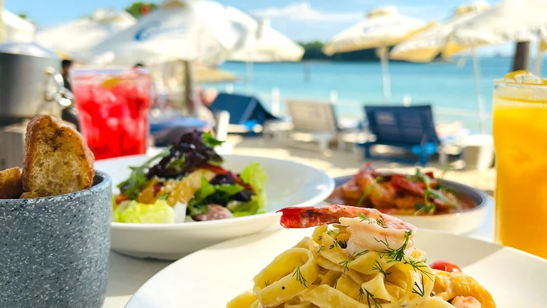 Pasta and salad dishes with drinks by a beachside setting, part of Food Discovery Pass.