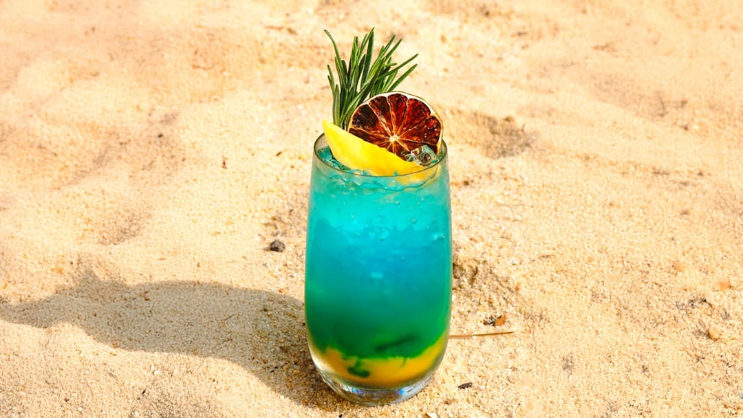 Tropical cocktail with citrus and herbs on sandy beach.