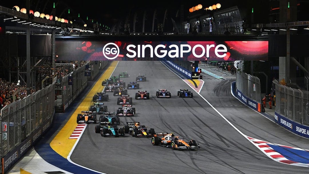 Formula 1 cars racing at night under Singapore sign during F1 Singapore Grand Prix.