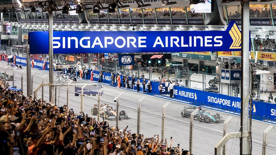 Formula 1 cars racing at Singapore Grand Prix 2025 with crowd in foreground.