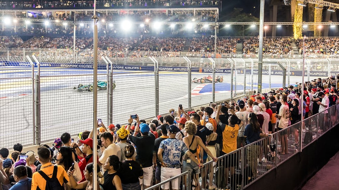 Crowd watching Formula 1 cars race at night during Singapore Grand Prix 2025.