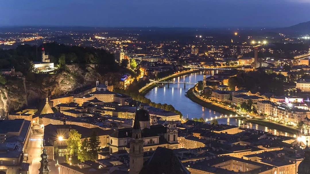 Fortress Hohensalzburg overlooking Salzburg at night with illuminated cityscape and river.