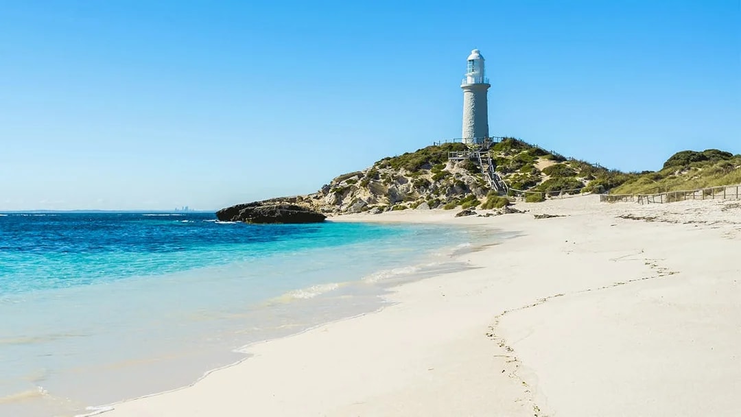 Lighthouse on Pink Beach, Rottnest Island, with clear blue water and sandy shore.
