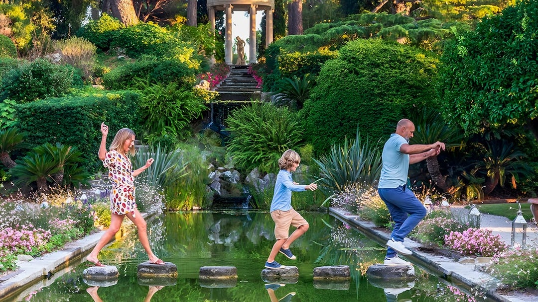 Family crossing stepping stones in a lush garden on the French Riviera.