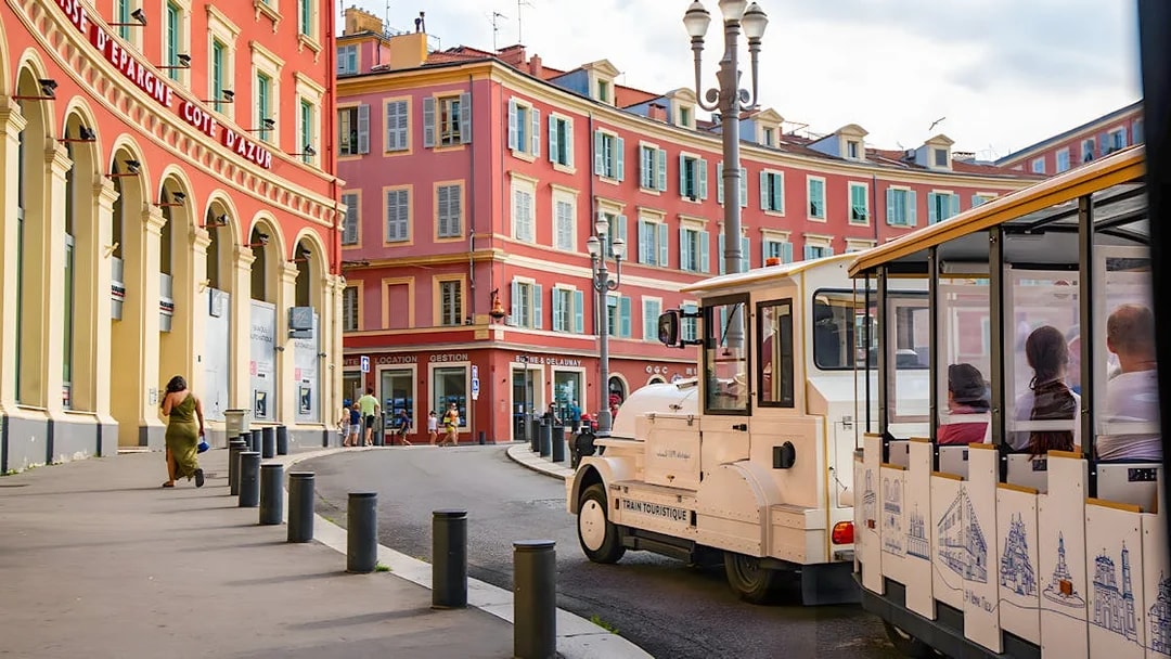 Tourist train passing colorful buildings in Nice, French Riviera.