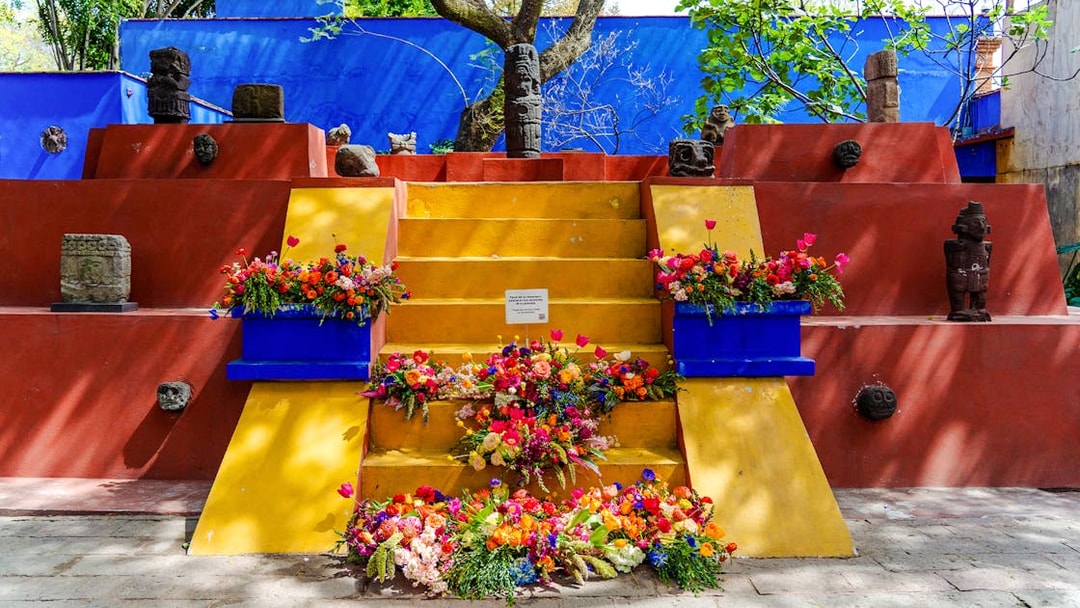 Yellow steps with colorful flowers and stone sculptures at Frida Kahlo Museum, Mexico City.