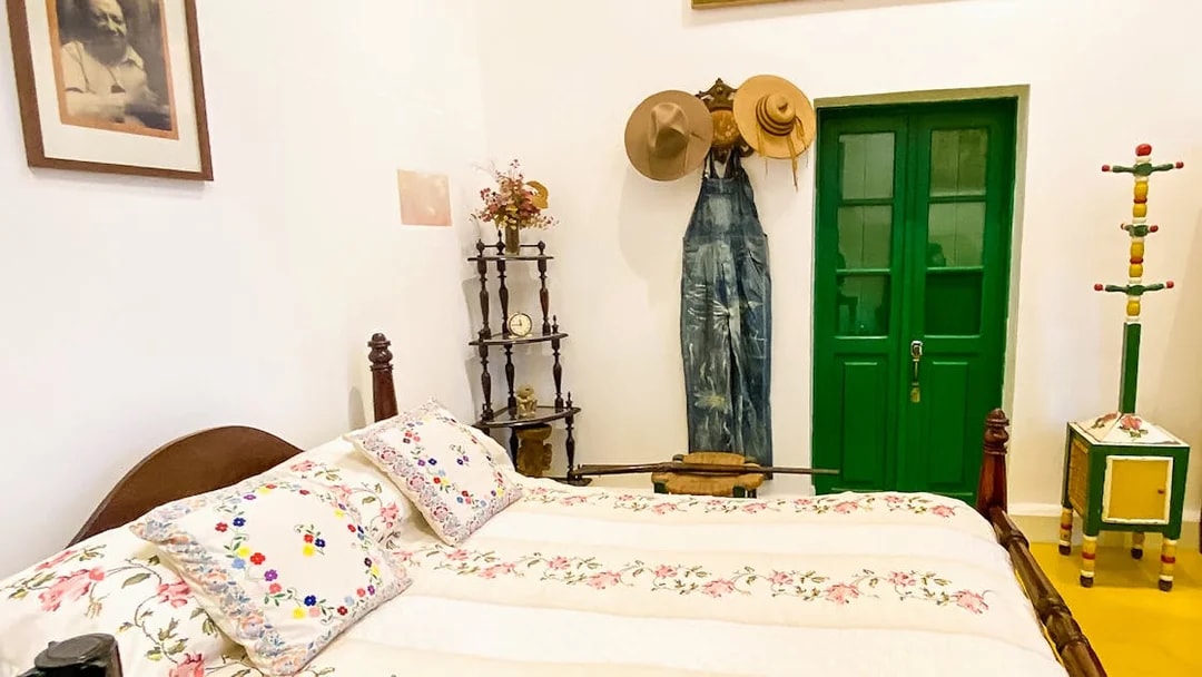 Frida Kahlo Museum bedroom with floral bedspread, green door, and hats on wall.