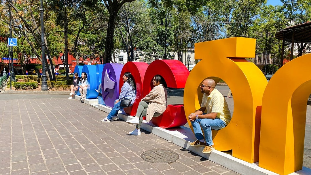 People sitting on colorful Coyoacán sign in a park setting.