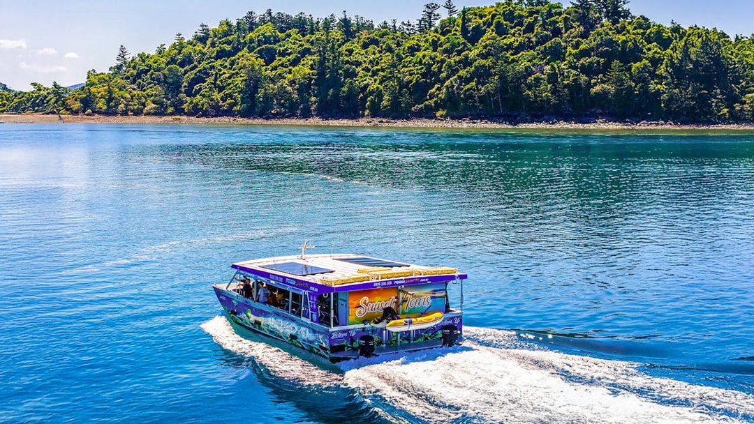 Glass bottom boat cruising near lush island at Airlie Beach.