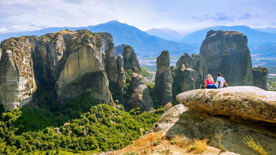 Couple sitting on rock overlooking Meteora rock formations, Greece.