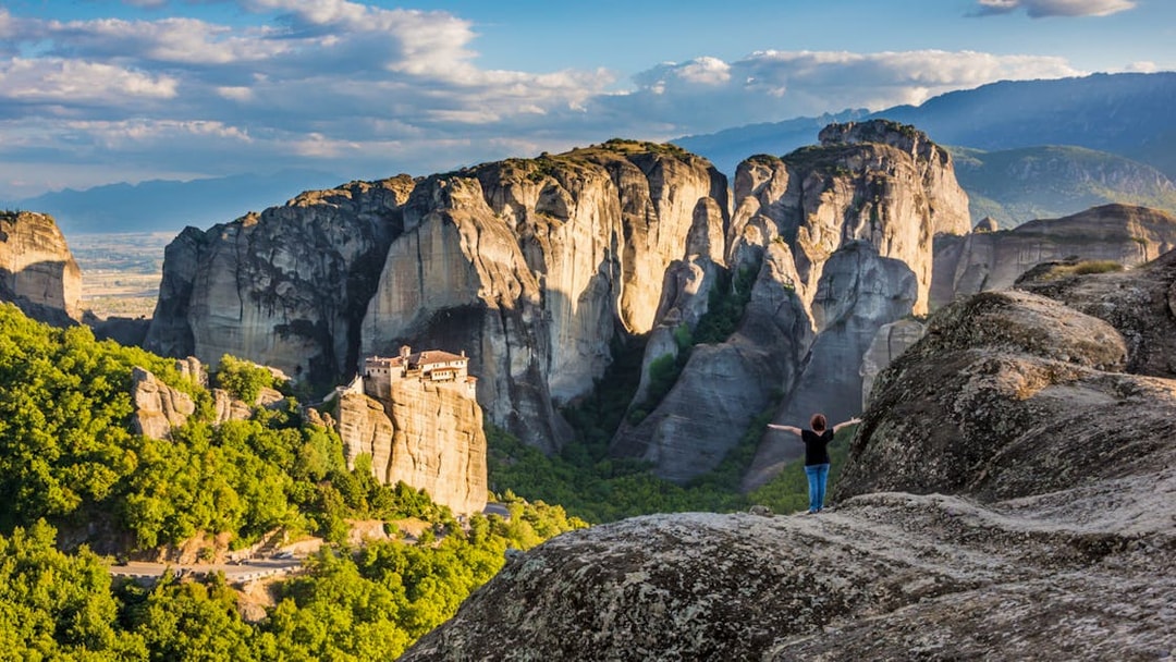 Meteora rock formations with monastery, person standing on cliff, Greece.