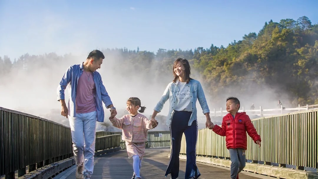 Family walking on a boardwalk through geothermal steam at Te Puia, Rotorua during a tour from Auckland.