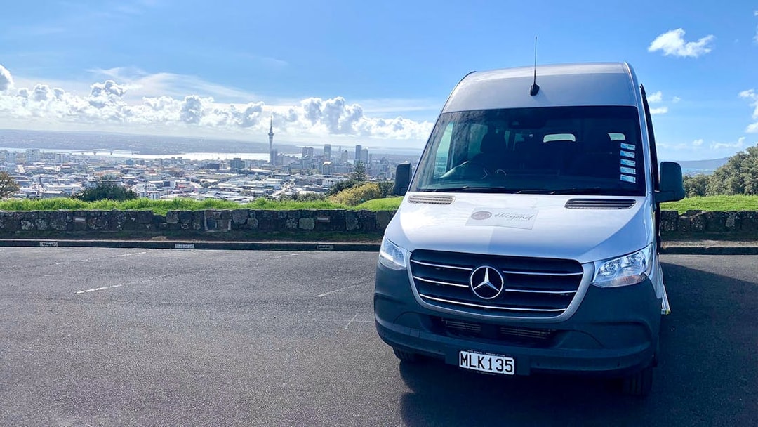Shuttle van in Auckland with city skyline, used for transfers to Hobbiton and Rotorua tours.