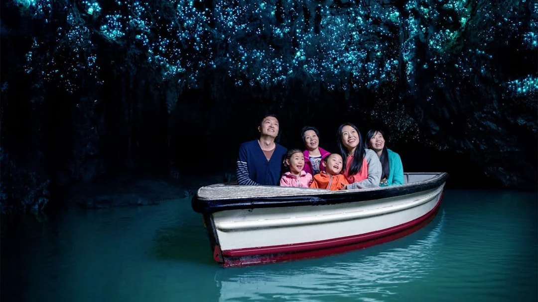 Group enjoying boat tour in Waitomo Glowworm Caves, New Zealand, with glowing ceiling.