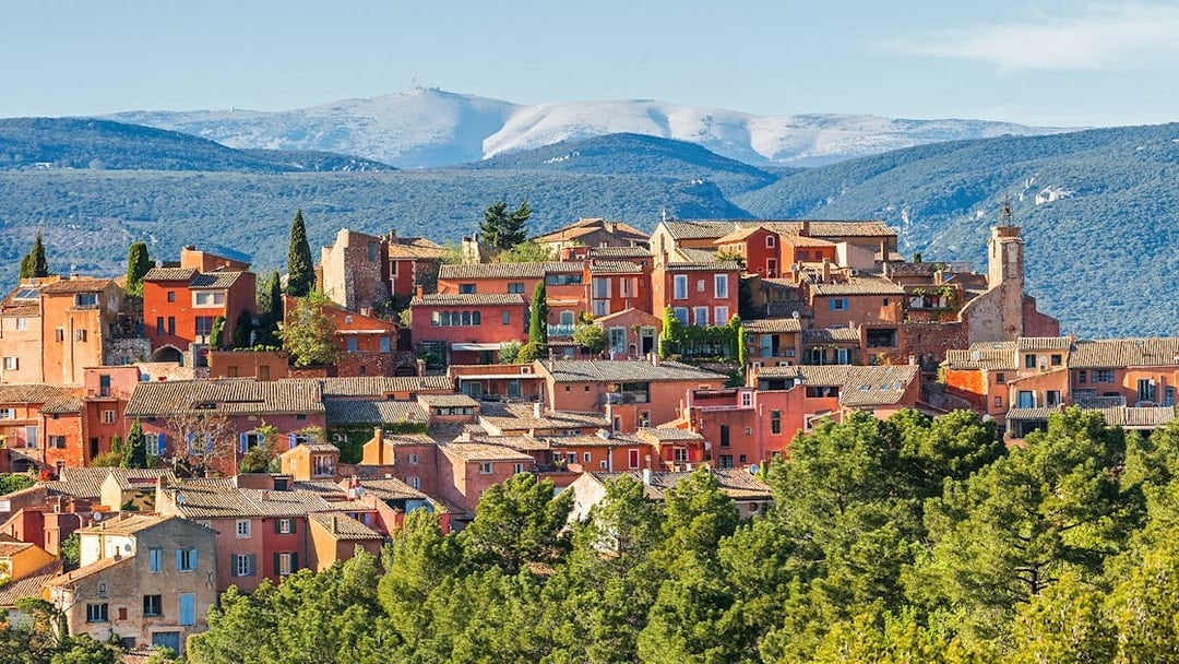 Roussillon village with ochre buildings in Provence, surrounded by green hills and distant mountains.
