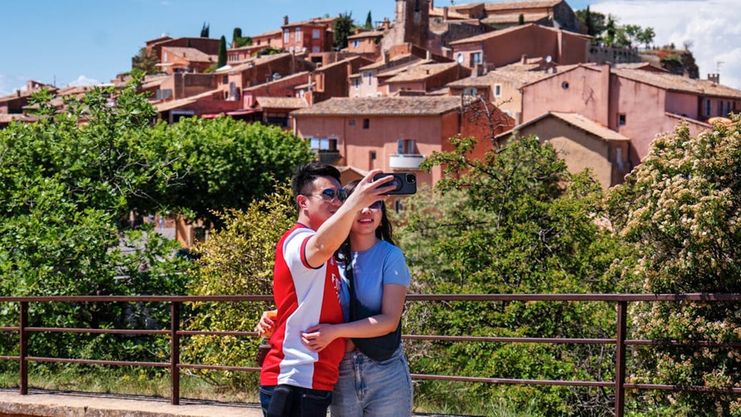 Couple taking a selfie with the colorful village of Roussillon, Provence in the background.