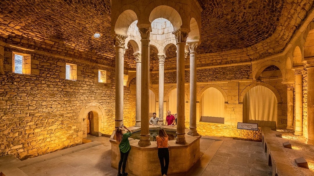 Tourists with guide in the Arab Baths of Girona, standing around central columns.