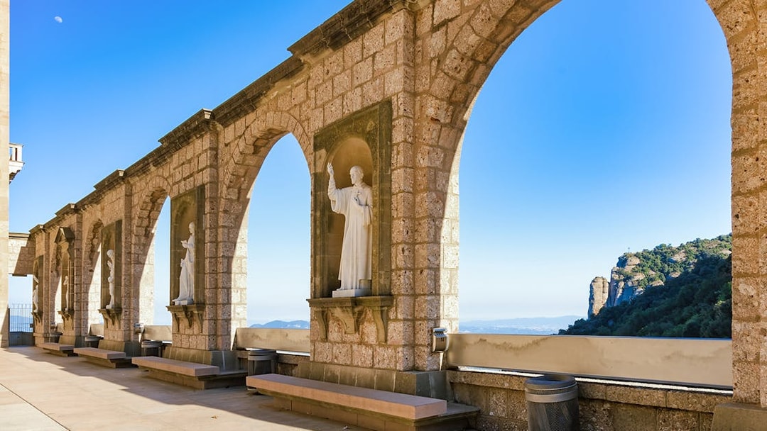 Stone arches and statues at Montserrat Monastery with mountain view, Spain.