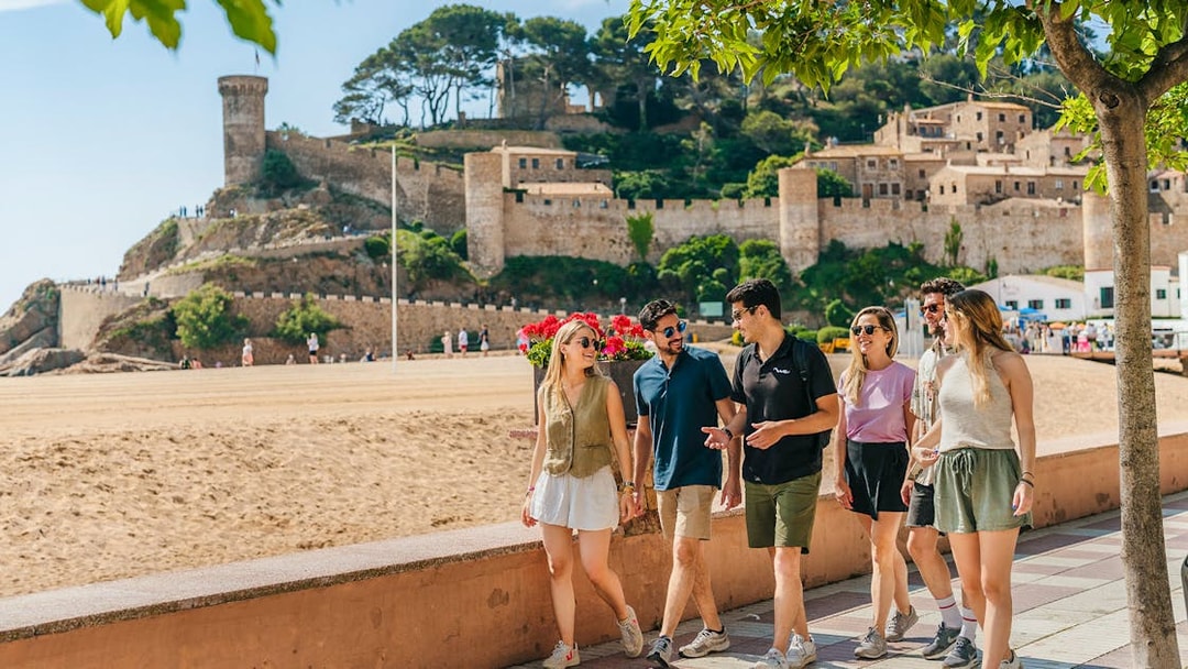 Tourists walking along the beach promenade near Tossa de Mar castle in Costa Brava.