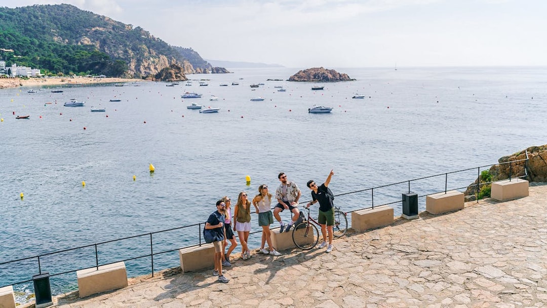 Tourists enjoying a scenic view of the Costa Brava coastline with boats in the water.