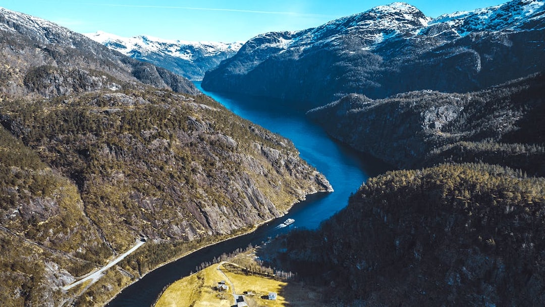 Cruise ship navigating through Mostraumen Fjord near Bergen, surrounded by steep cliffs and snowy peaks.