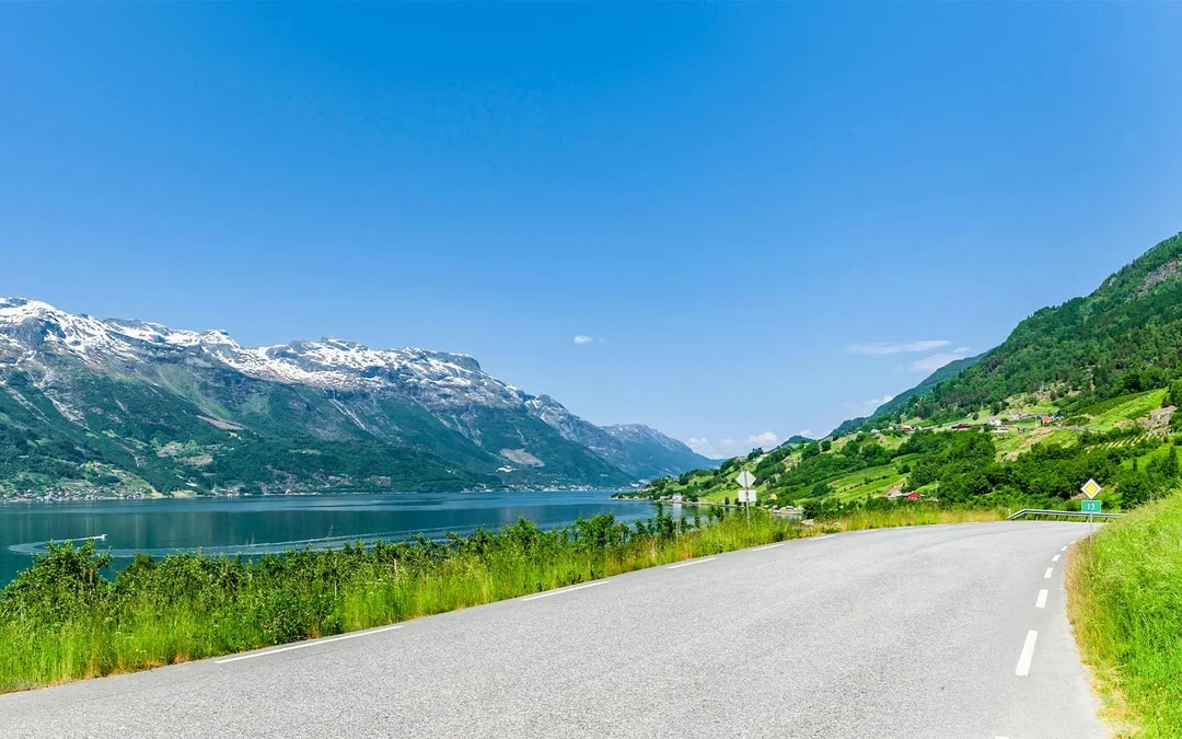 Scenic road along Hardangerfjord with mountains and clear blue sky.