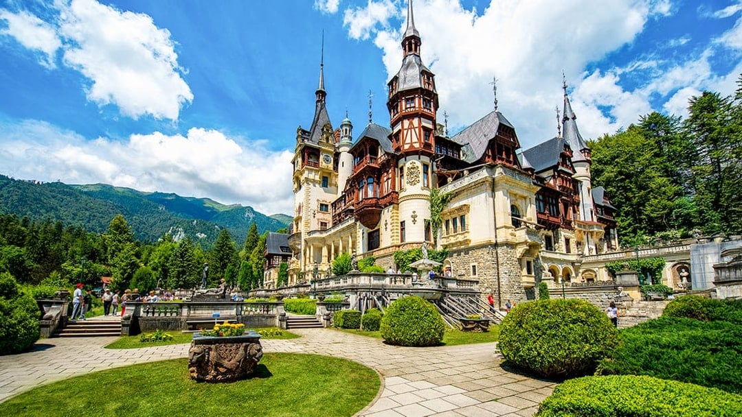 Peles Castle exterior with gardens and Carpathian Mountains in Sinaia, Romania.