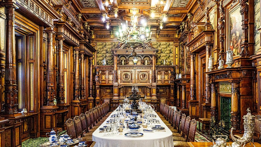 Elegant dining room inside Peles Castle with ornate woodwork and a long table set for a banquet.