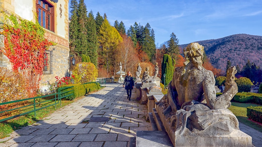 Guests walking along the garden path at Peles Castle, Romania, with statues and autumn foliage.