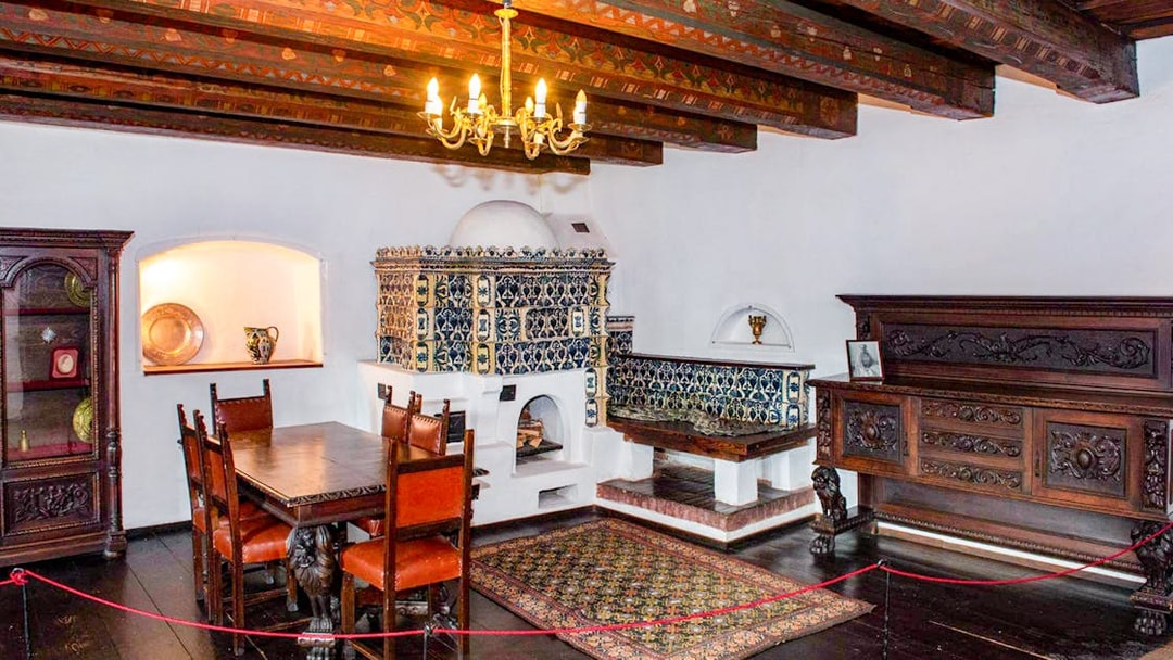 Dining room with ornate wood furniture and tiled stove inside Bran Castle, Romania.