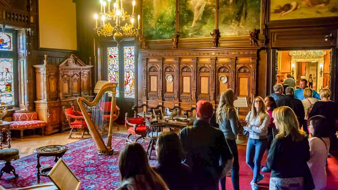 Visitors exploring the music room at Peles Castle with ornate woodwork and stained glass windows.