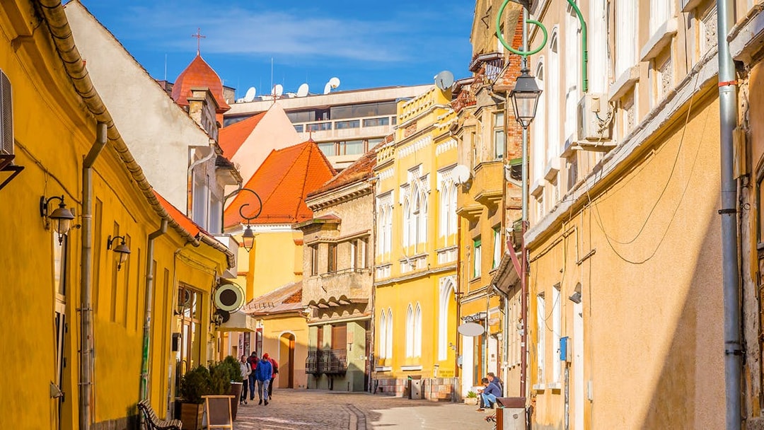 Street view of colorful historic buildings in Old Town, Brasov, with people walking.