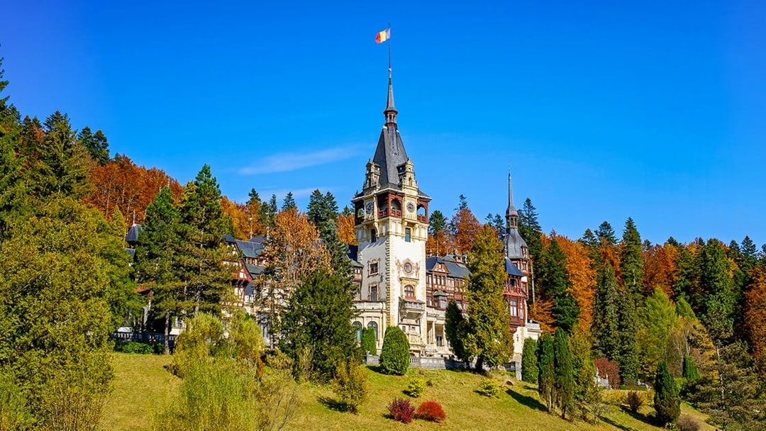 Peles Castle with ornate architecture surrounded by autumn trees in Sinaia, Romania.