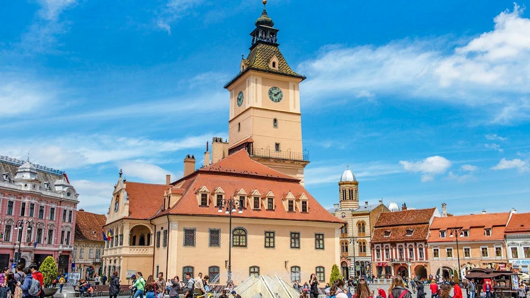 Medieval clock tower in Brașov's Council Square with tourists exploring.