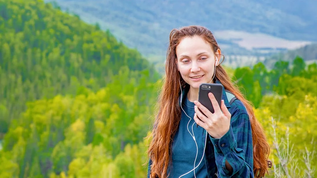 Woman using audio guide on smartphone in a lush green forest setting.