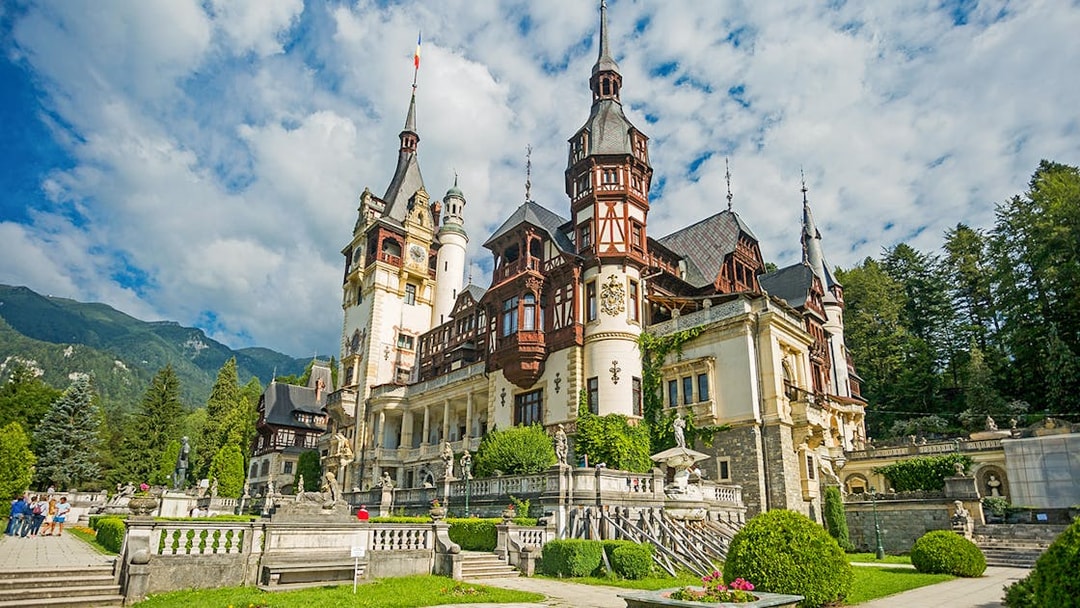Peles Castle exterior with ornate towers and lush gardens in Sinaia, Romania.
